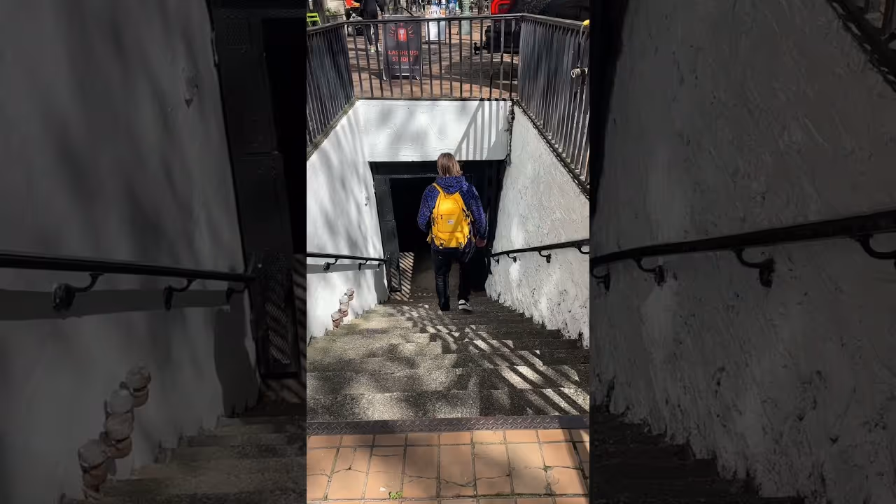 Person with yellow backpack walking down outdoor stairs into a dark underground space.