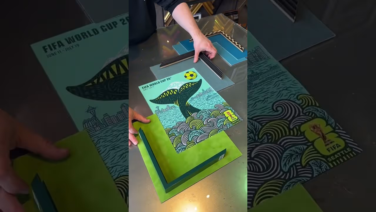 Person framing a colorful FIFA World Cup 2026 poster featuring a whale tail and ocean waves.