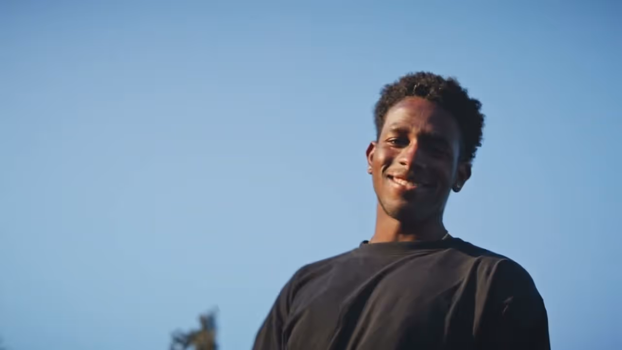 Smiling young man in a black shirt outdoors with clear blue sky background.