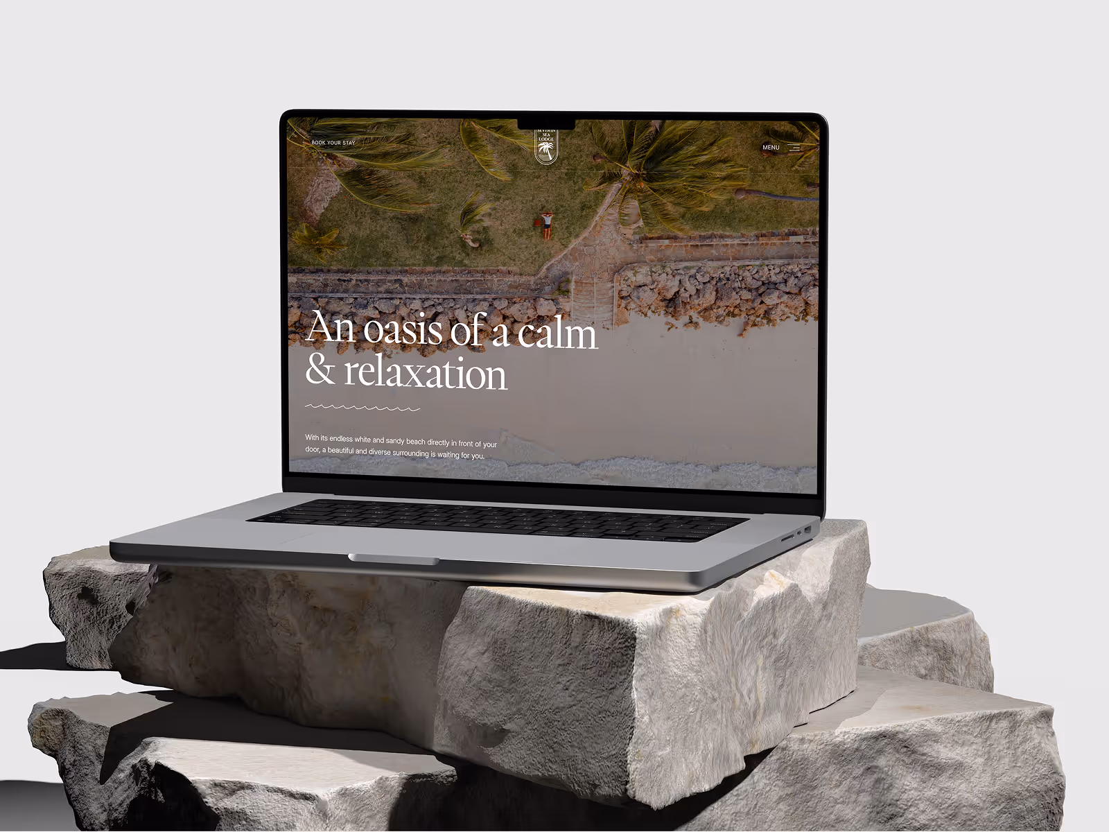 Laptop displaying a website with aerial view of a beach, palm trees, and a person lying on grass, with text reading 'An oasis of calm & relaxation'.