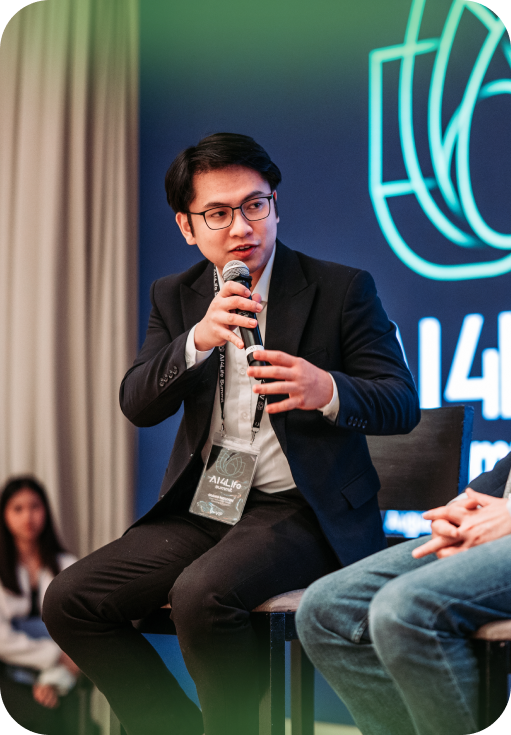Man in a dark suit and glasses speaking into a microphone during a panel discussion.
