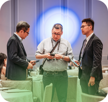 Man in black jacket walking between tables while audience in business attire claps in a conference room.
