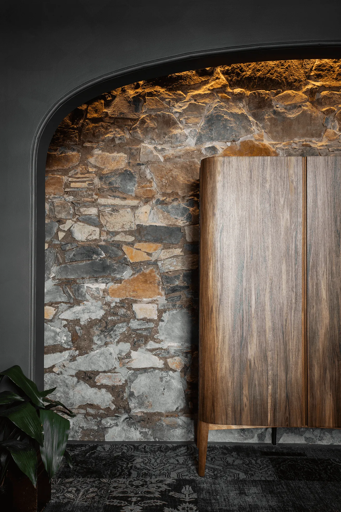 A stone wall, with a wooden, beautifully crafted cabinet.