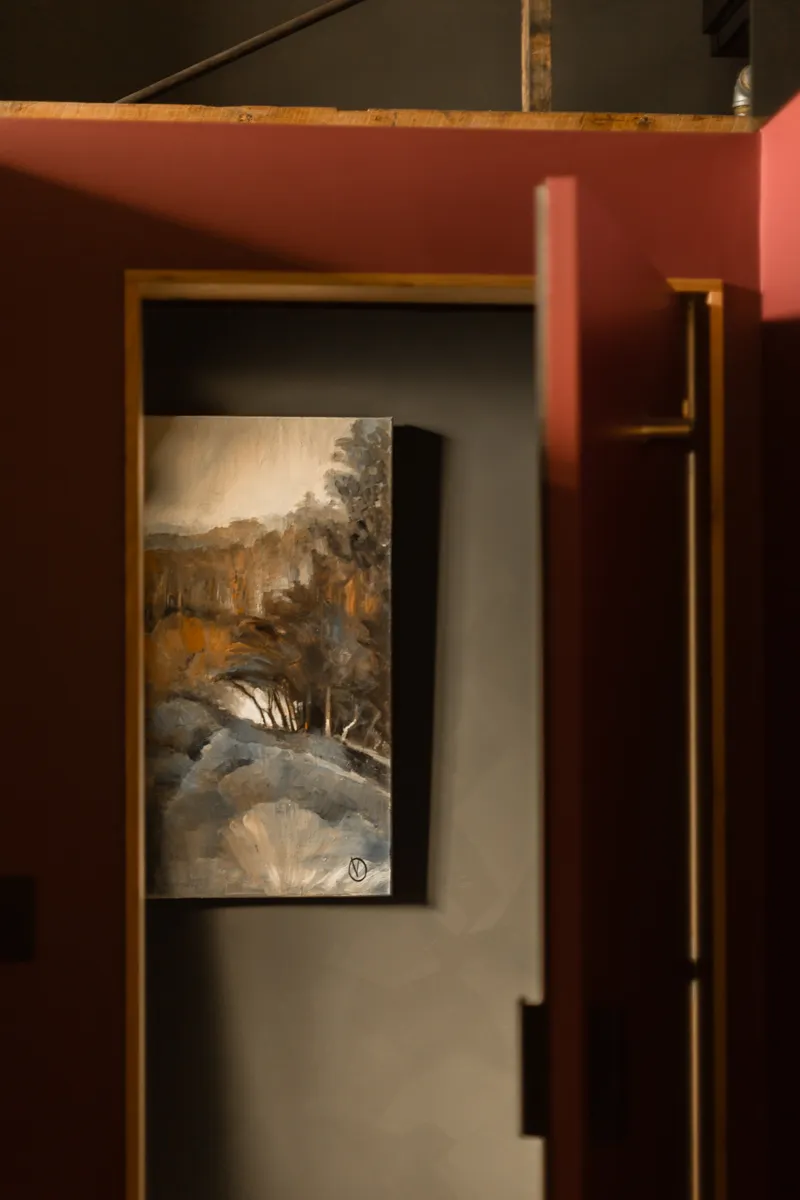 A doorway with red painted walls, and a beautiful landscape painting. 