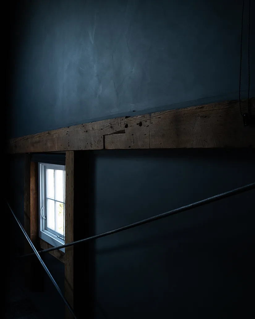 Window overlooking the water, surrounded by moody walls and wooden beams.