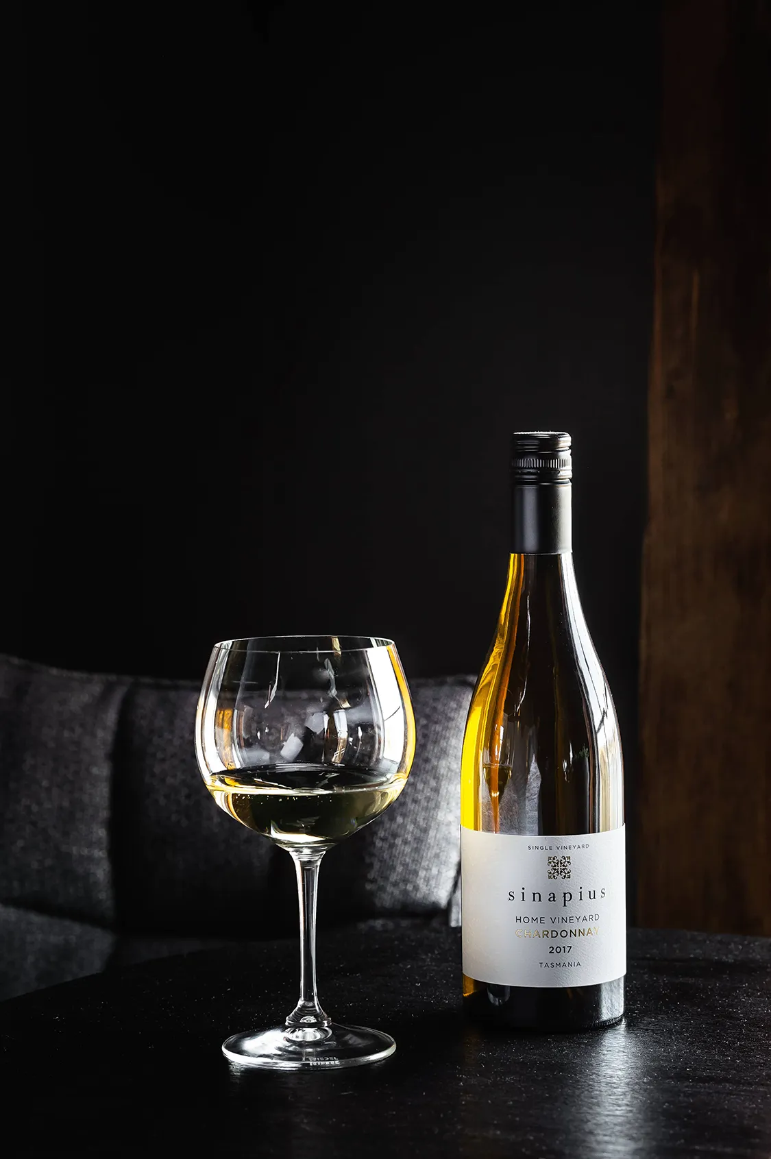 A couple sits in front of a window overlooking the river. The lighting is romantic and moody, and they are celebrating a special occasion with wine. 