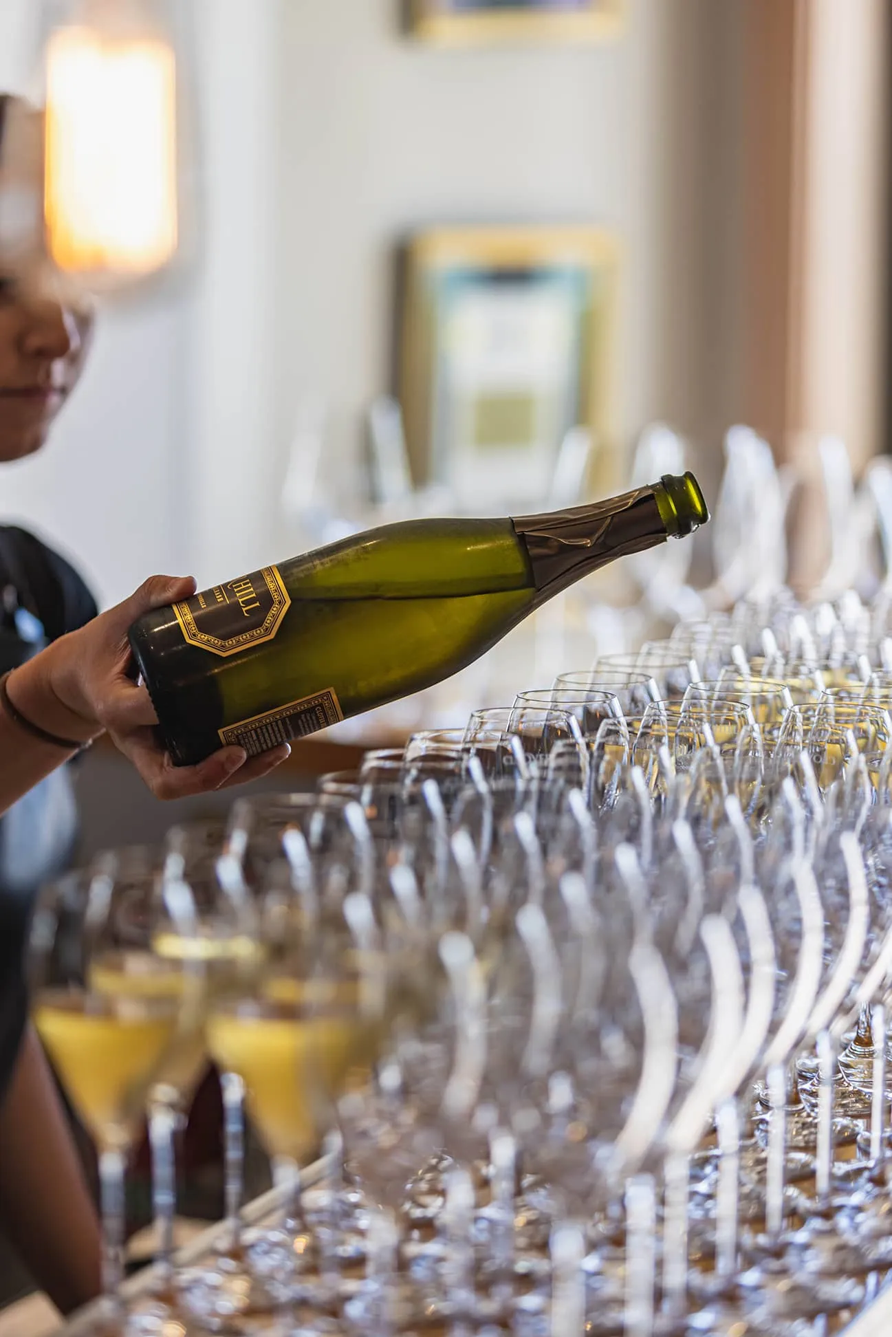A sea of champagne flutes in setup on the table, with a bottle of bubbles being poured. 