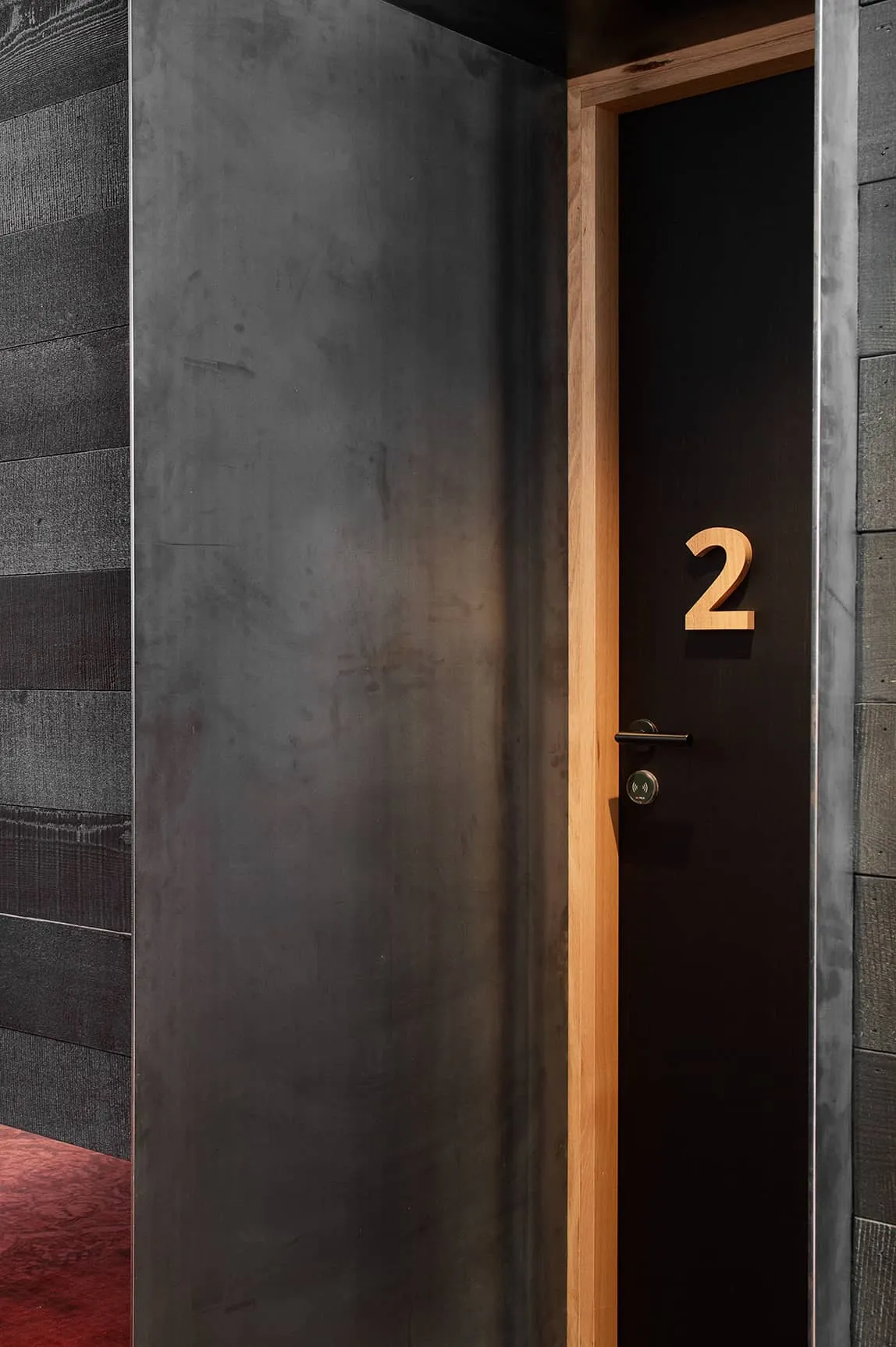 A grey metallic wall, with a wooden door, with the number 2 on it. 