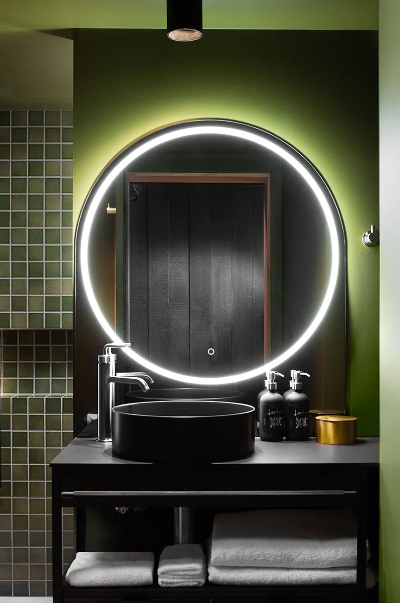 A bathroom mirror mounted on the wall above a sink, with a tap and plumbing fixtures visible. The indoor space is well-lit.