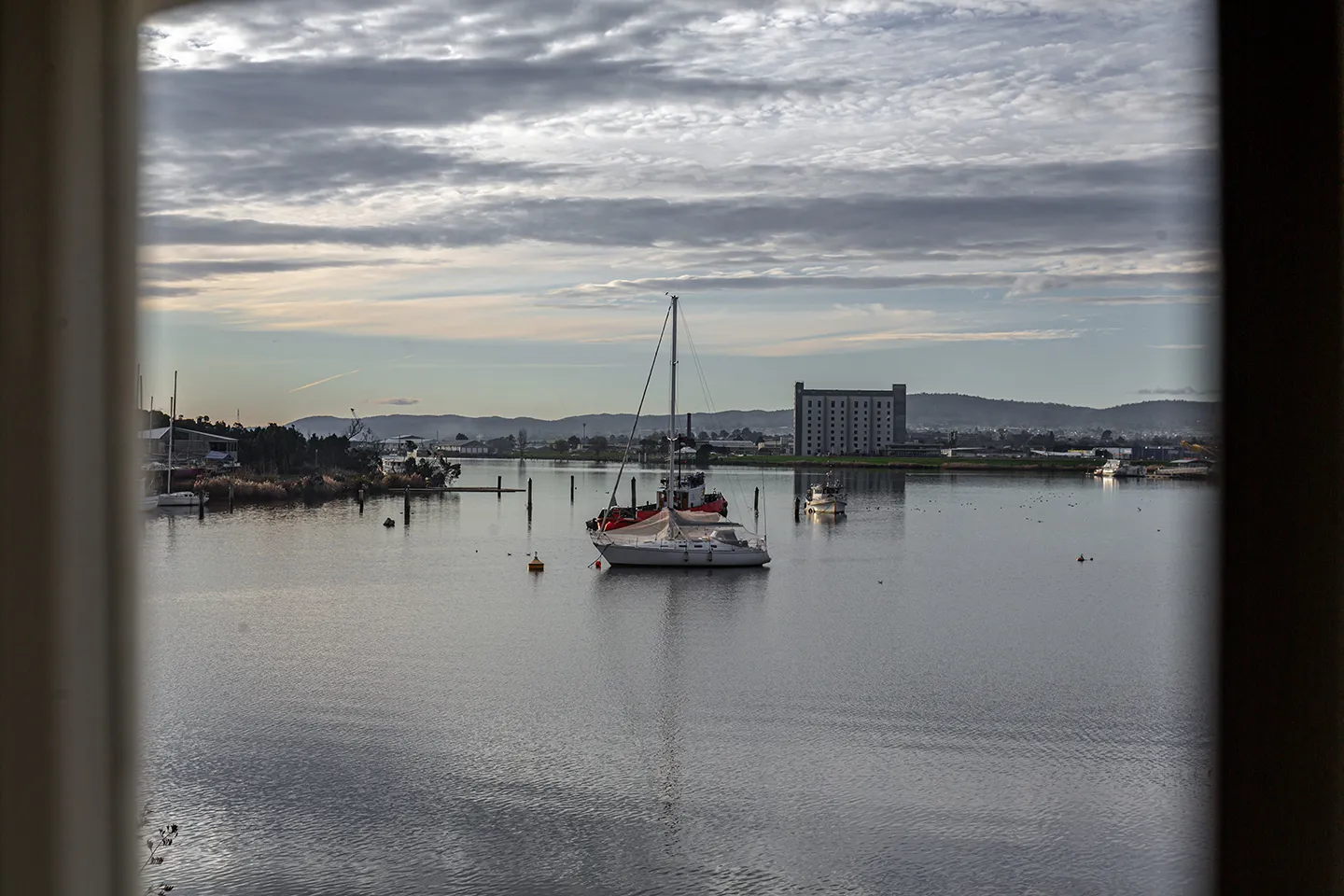 A river view in portrait. Boats and relfection on the water. Buildings and hills in the background. It is a fine, cloudy day. 
