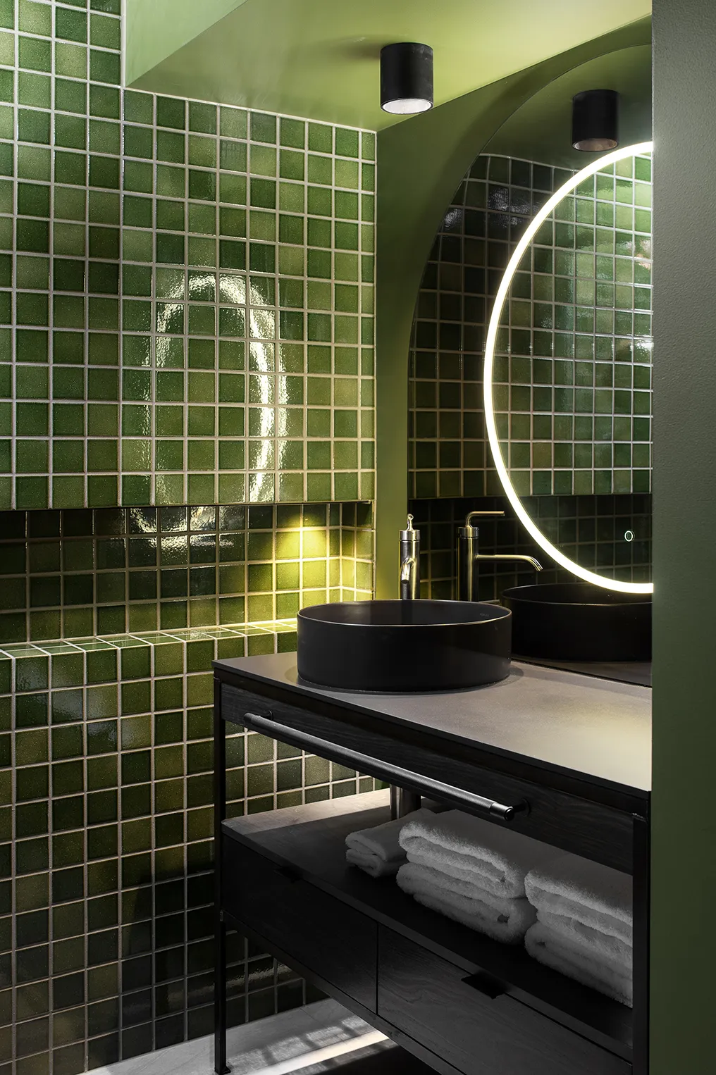 A spacious bathroom featuring a large wall mirror above a sink, with tiled walls and floor. The space includes a shower, toilet, and various plumbing fixtures.
