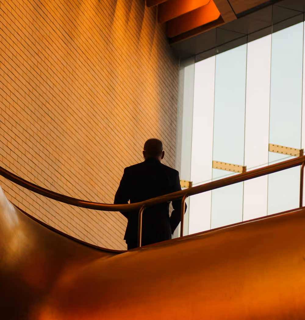 Un homme en costume noir vu de dos, debout près d'une rampe dans un bâtiment moderne.