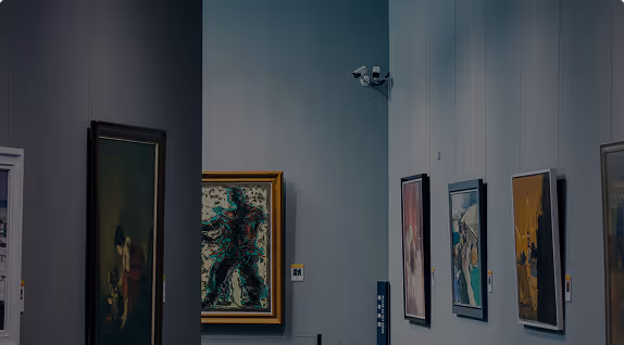 Vue intérieure d'une galerie d'art avec des tableaux colorés accrochés aux murs sous une lumière tamisée.