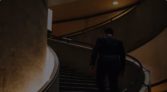 Homme en costume montant un escalier courbe dans un environnement sombre et élégant.