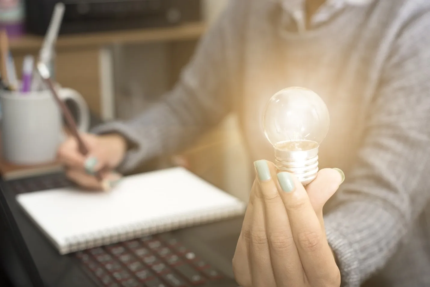 A lightbulb lit up in someone's hand working at a desk.