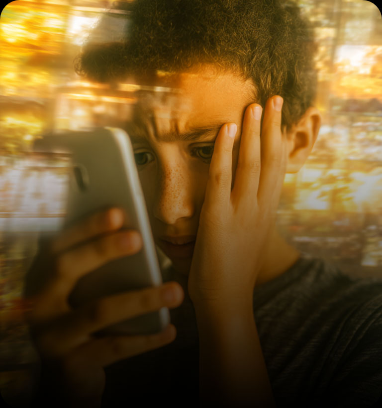 Chłopiec trzyma telefon komórkowy, siedząc długo przed ekranem, skupiony na treści.