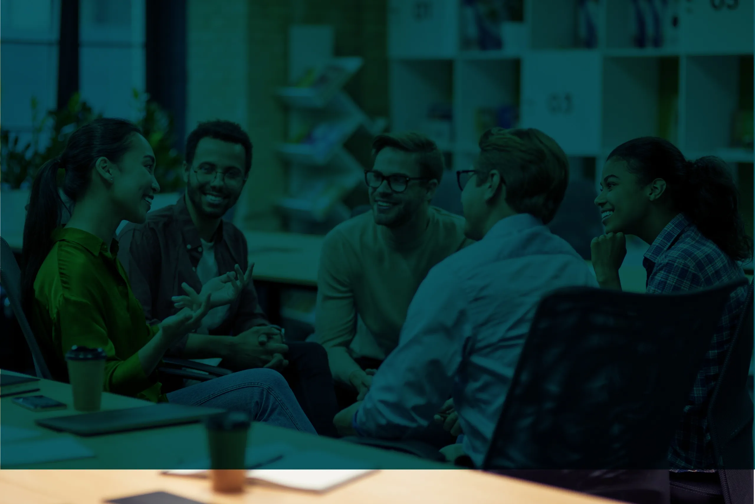 Five young professionals sitting and smiling during an informal group discussion in a modern office setting.