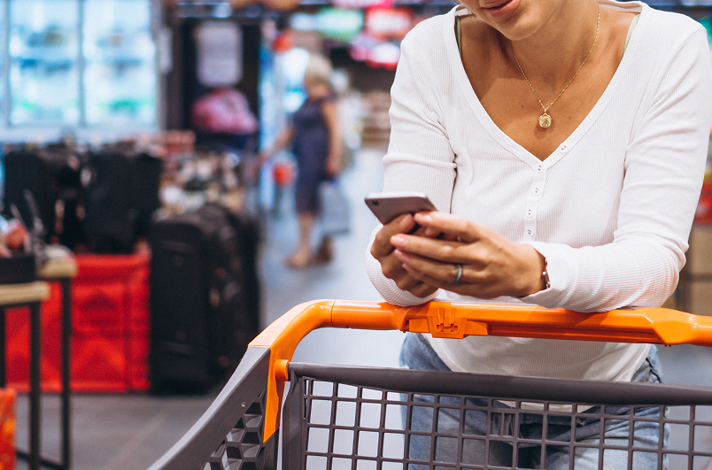 A man looks at a flower in a pot, glancing at a woman through a flower-filled alley in a shop.