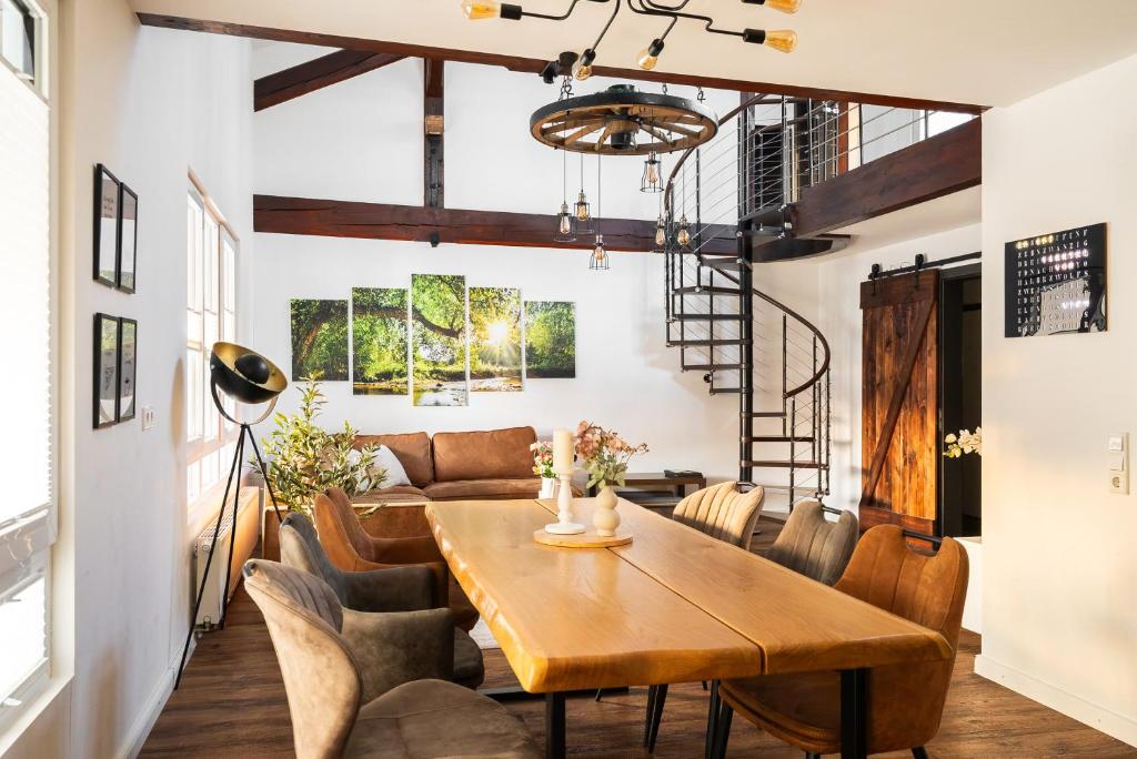 Helles Esszimmer mit großem Holztisch, gepolsterten Stühlen, Ledersofa, spiralförmiger Metalltreppe und Wanddeko mit Naturmotiven.