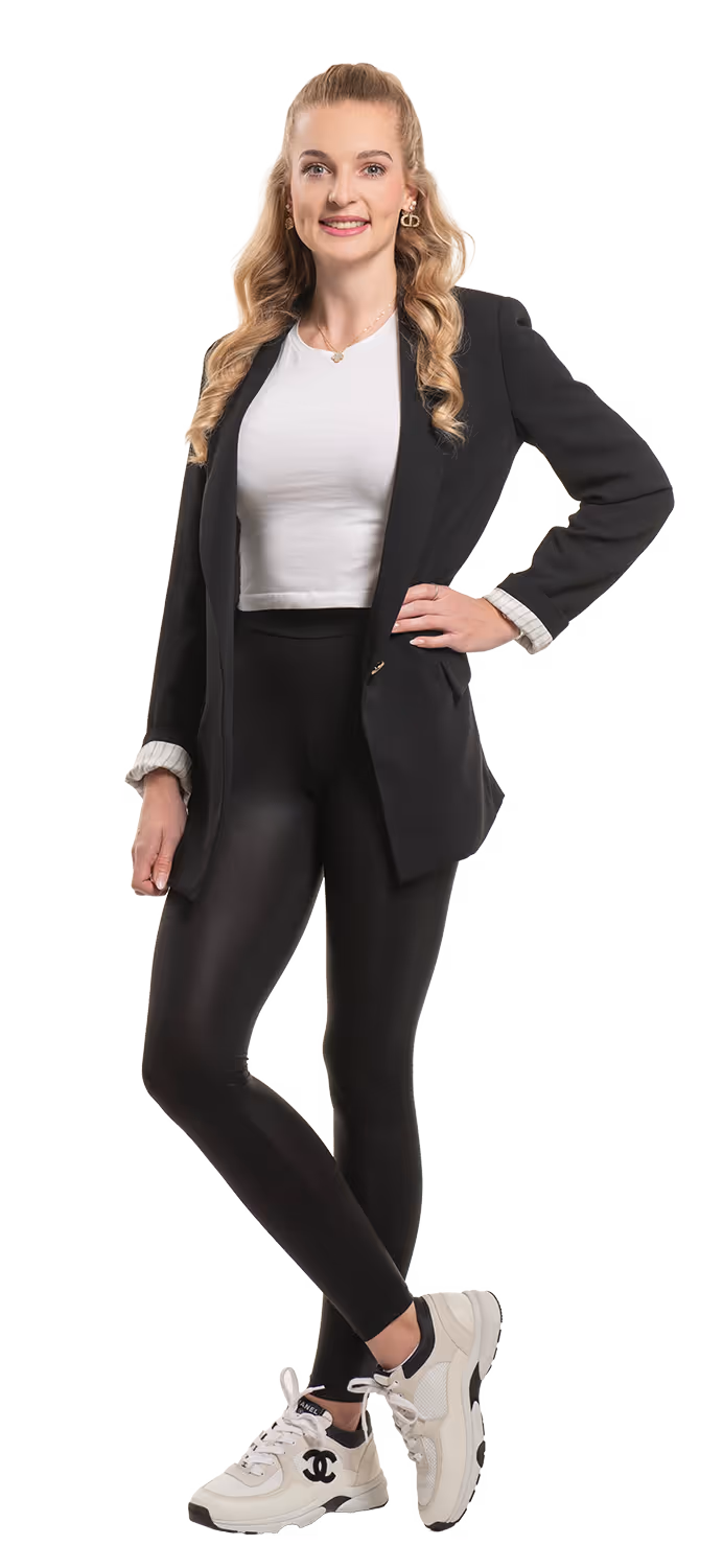 Junge Frau mit langen, lockigen blonden Haaren in schwarzem Blazer, weißem T-Shirt, schwarzen Leggings und weißen Sneakern.