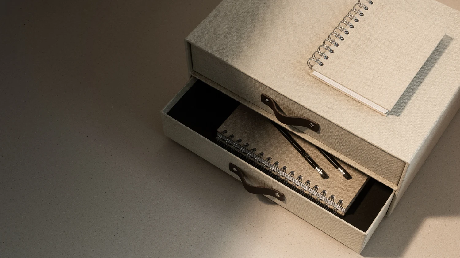 Bigso 2025 catalog storage collection — beige linen-covered drawer box with leather handles, paired with spiral notebooks and pencils, showcasing sustainable Scandinavian design for modern organization.