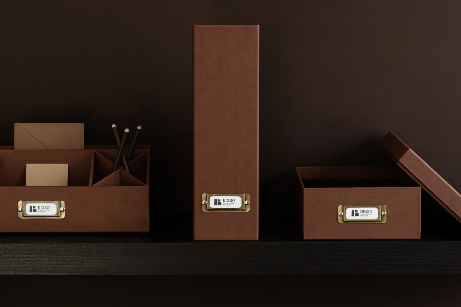 Bigso recycled leather office organizers in brown, including magazine file holder, storage box, and desk organizer with brass label holders, for sustainable workspace storage.