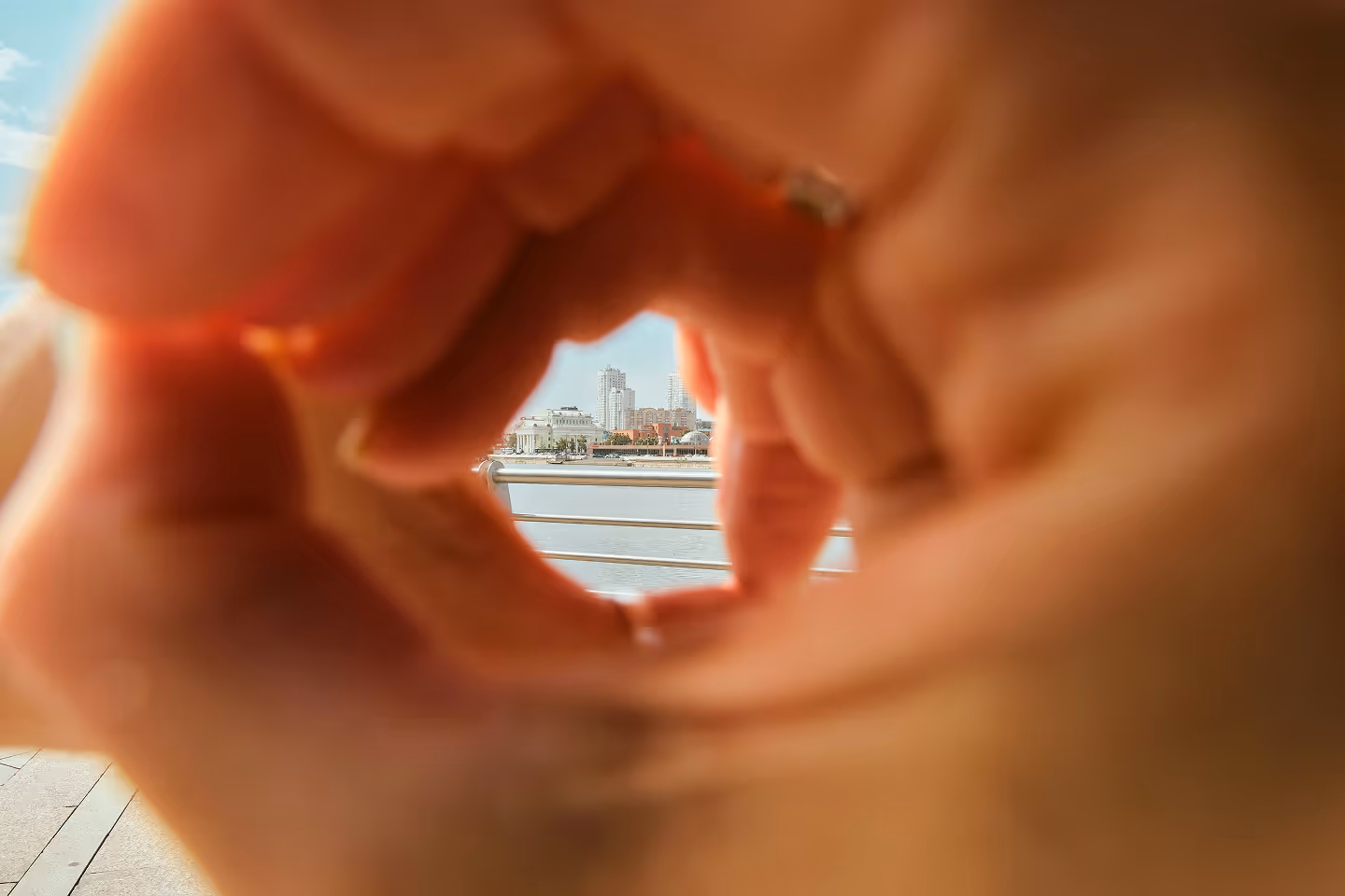 Vue d'une ville au bord de l'eau encadrée par une forme de cœur faite avec les mains floues au premier plan.