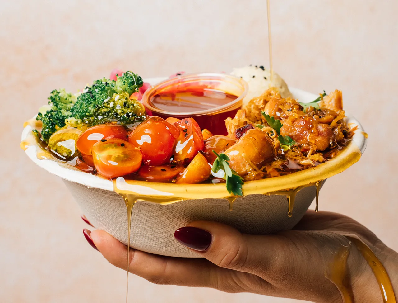 person holding salad bowl with honey dressing dripping onto it from above