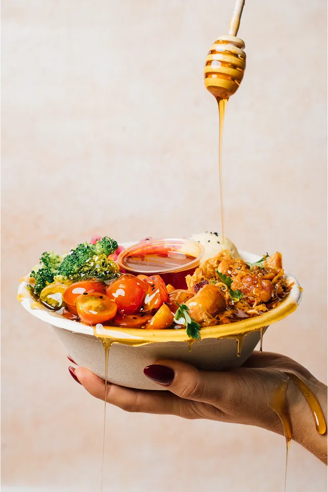person holding salad bowl with honey dressing dripping onto it from above