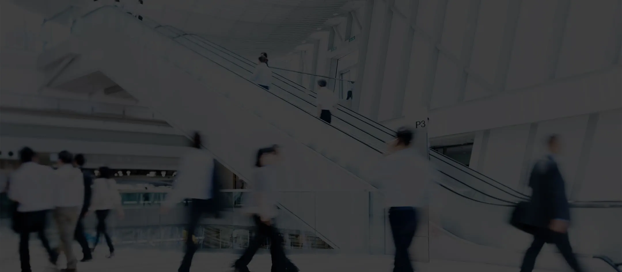 A group of people walking down a street next to an escalator.