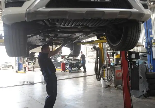 Mechanic inspecting the underside of a car lifted on a hydraulic vehicle lift in an auto repair shop.