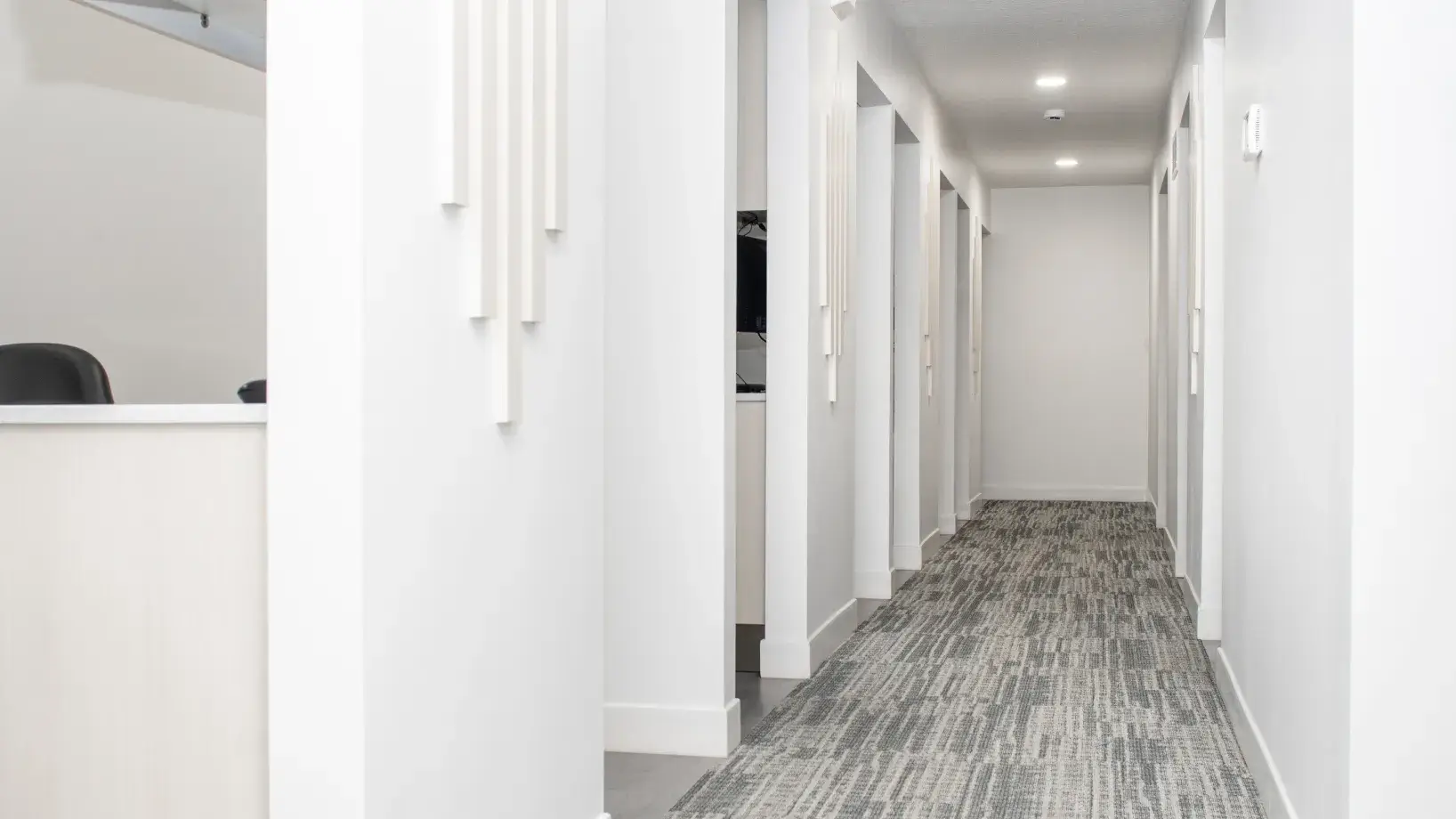 Bright hallway with gray patterned carpet, white walls, and open doorways on the right side.