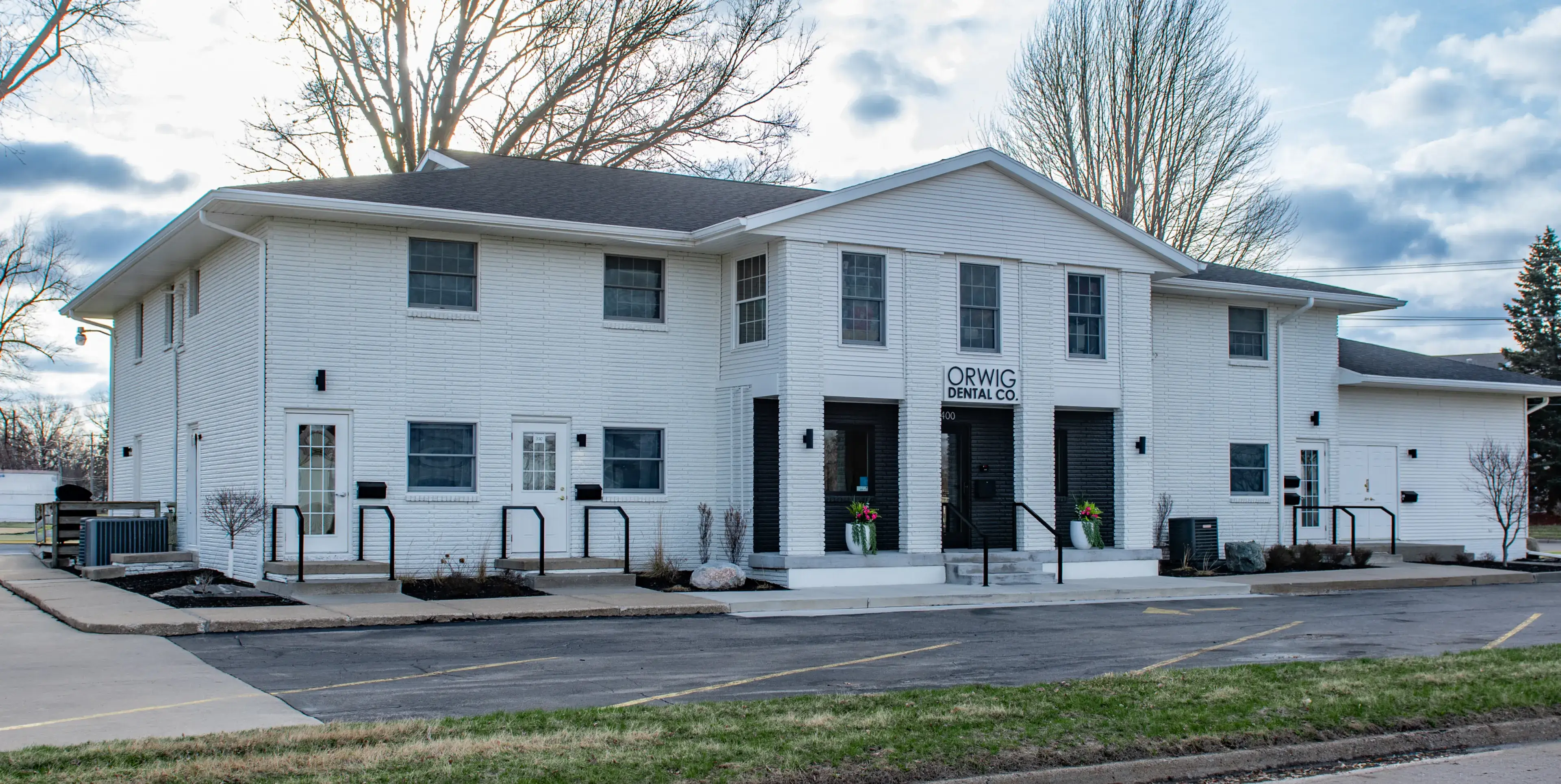 Two-story white brick building with Orwig Dental Co. sign above the main entrance and parking spaces in front.