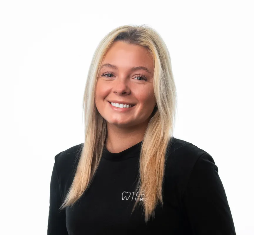 Smiling woman with long blonde hair wearing a black shirt with a tooth logo and 'Dental' text.