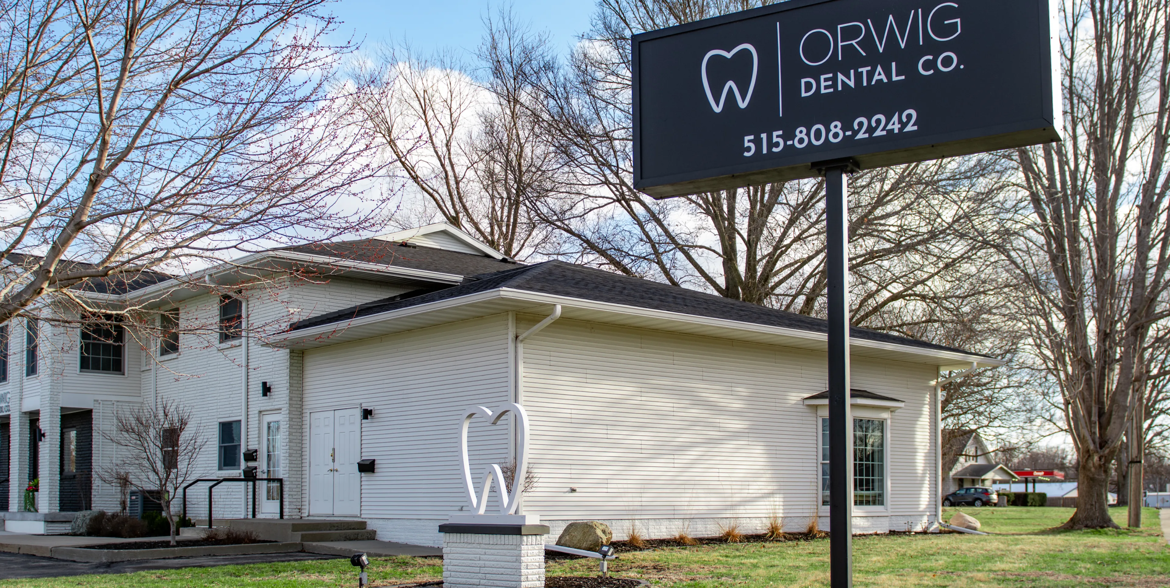 White building with a black sign reading 'Orwig Dental Co.' and phone number 515-808-2242, featuring a tooth-shaped sculpture in front.