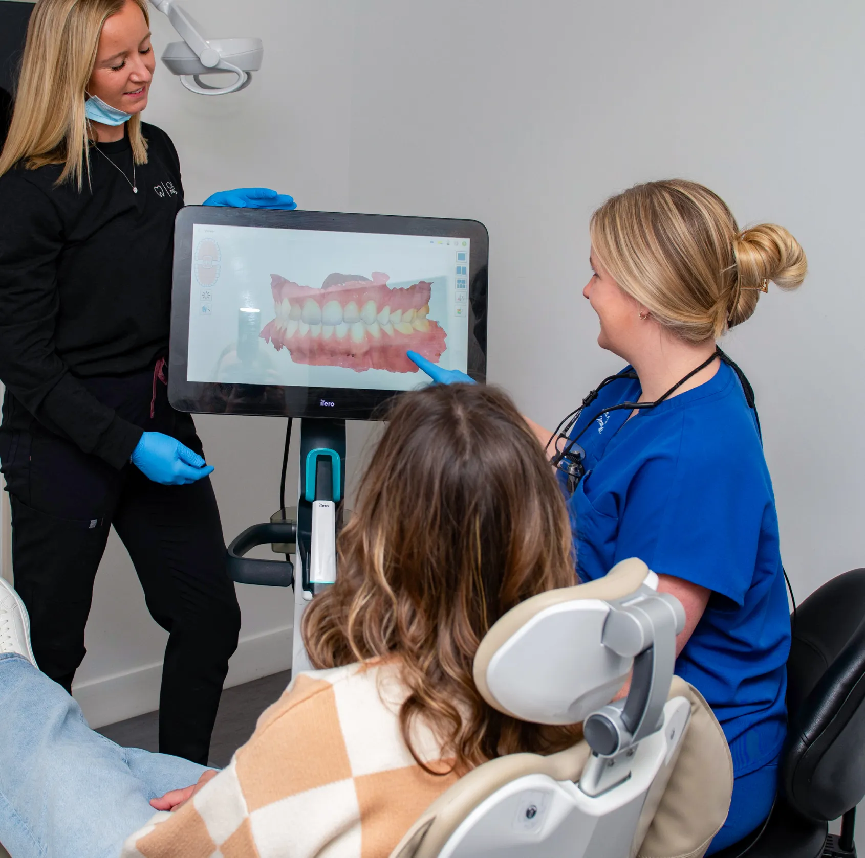 Two dental professionals showing a digital 3D dental scan on a screen to a patient seated in a dental chair.