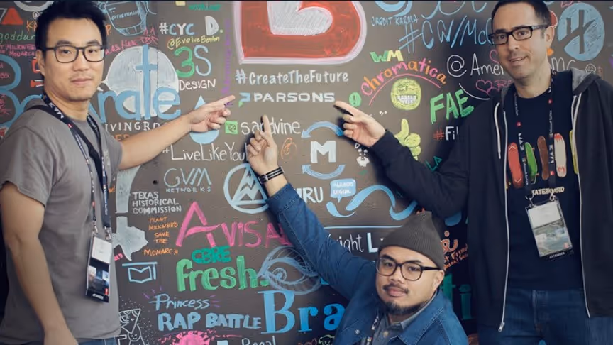 Three people posing with colorful graffiti wall of creative logos and text