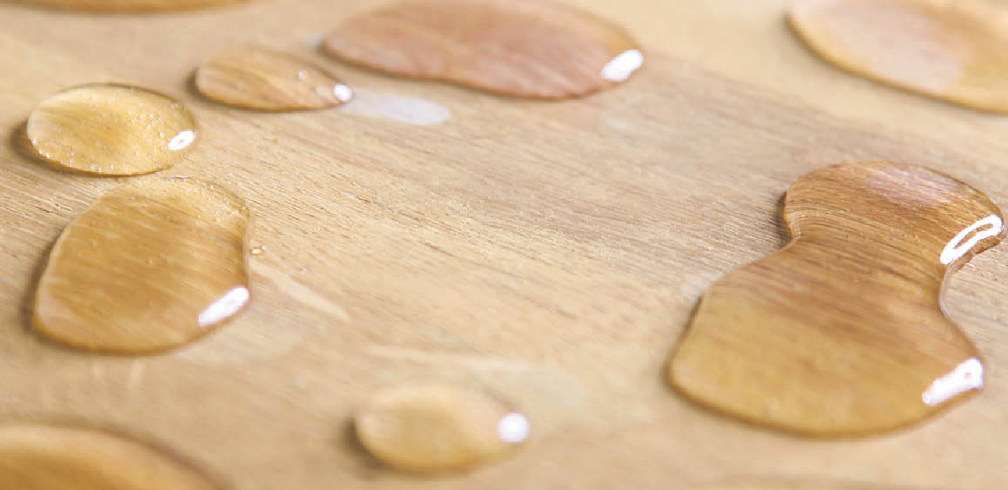 Water droplets resting on a wood surface.