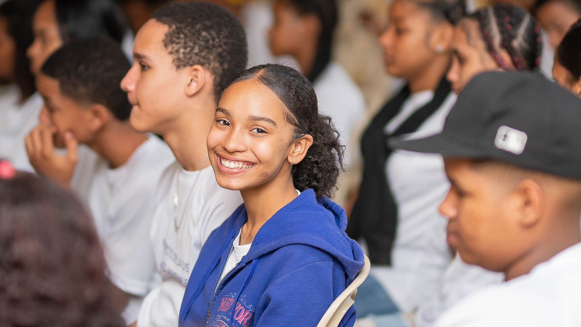 Joven con camiseta oscura y mochila mirando hacia una ventana iluminada en un espacio interior.