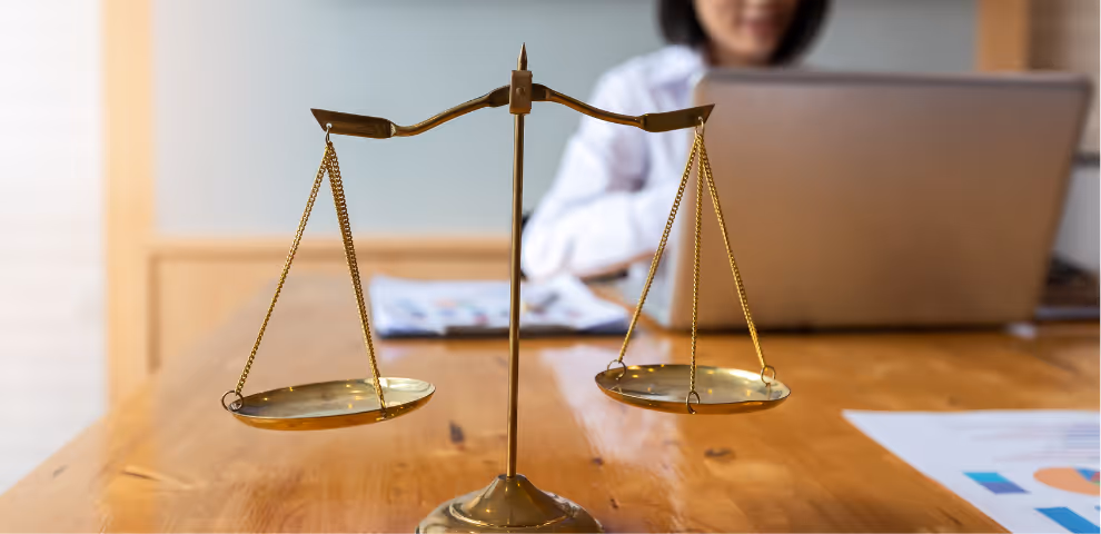 Image of justice scale with woman on her laptop in the background