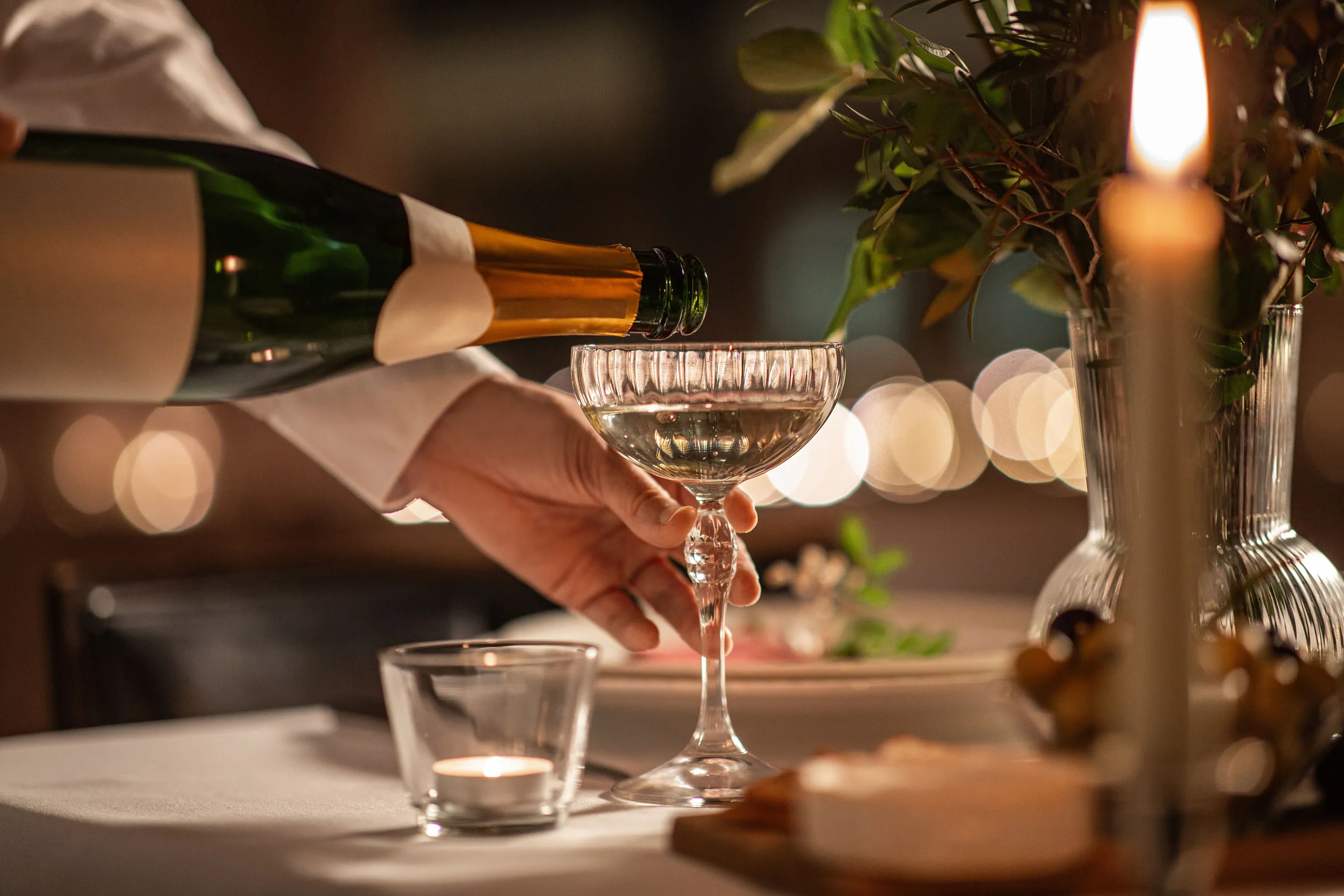 Someone pouring a champagne-like drink into a glass in a candlelit ambience