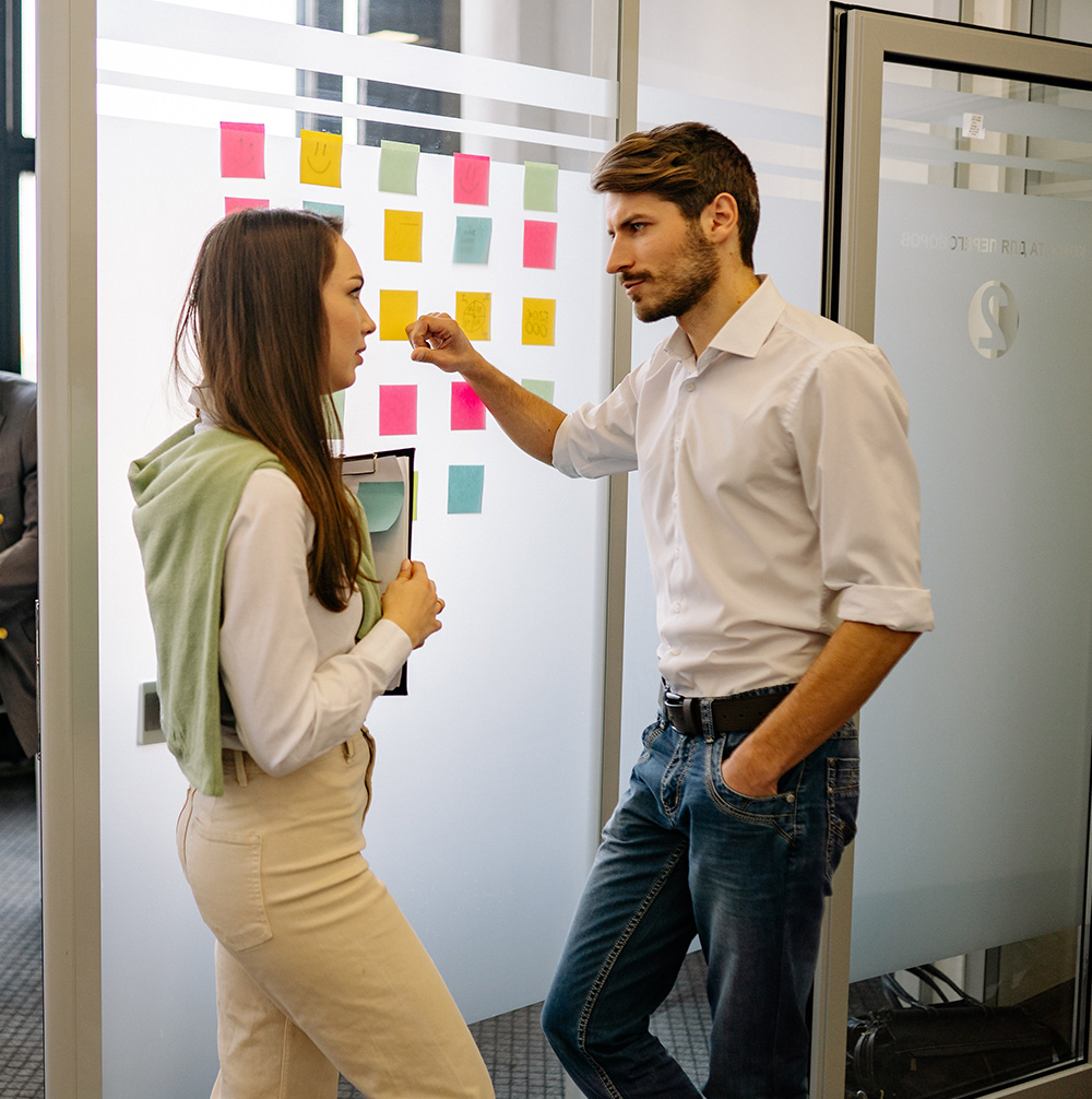 Two coworkers discuss project in office hallway.