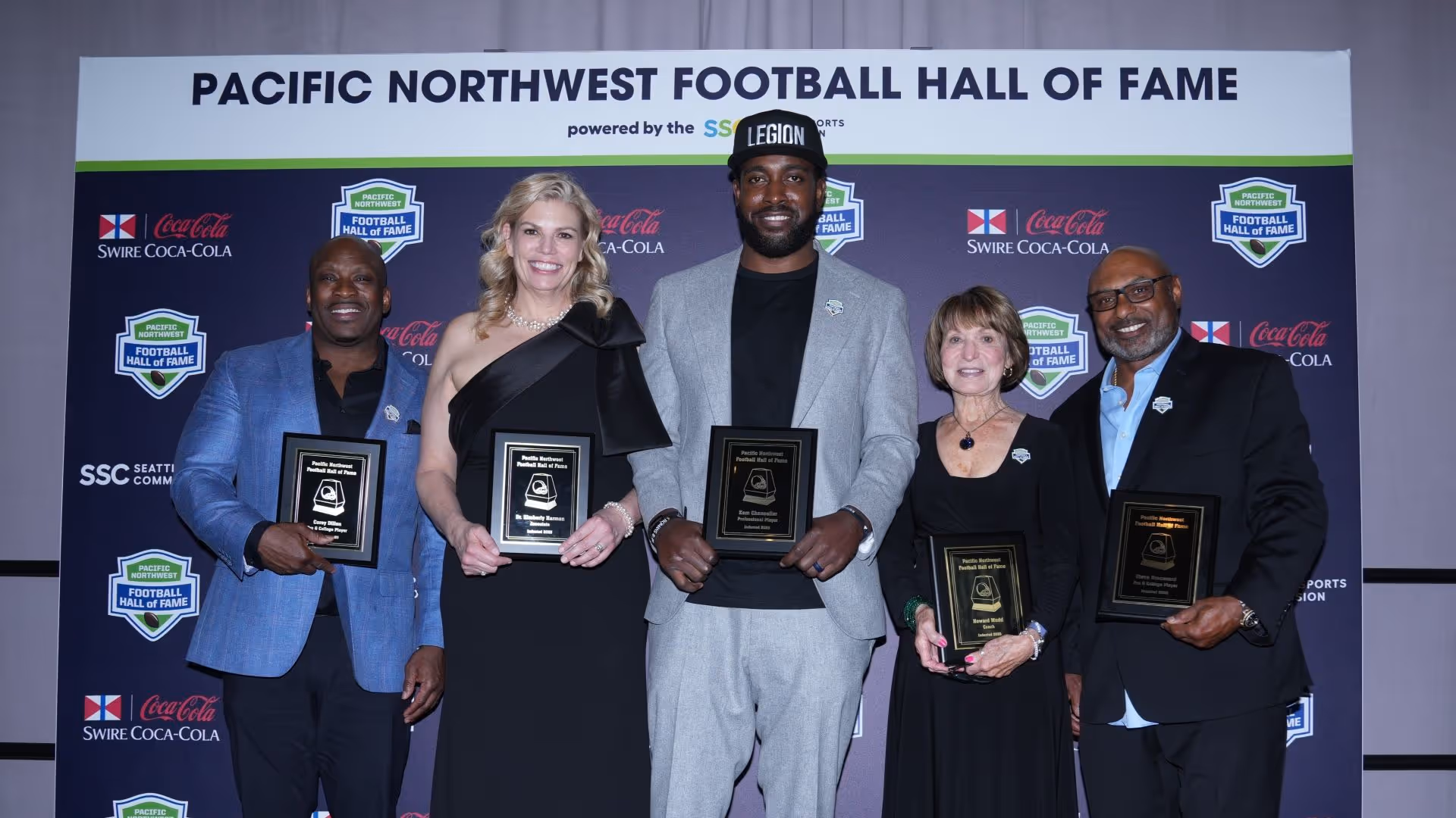 Five Pacific Northwest Football Hall of Fame inductees standing in front of a Hall of Fame backdrop, each holding a plaque and smiling.