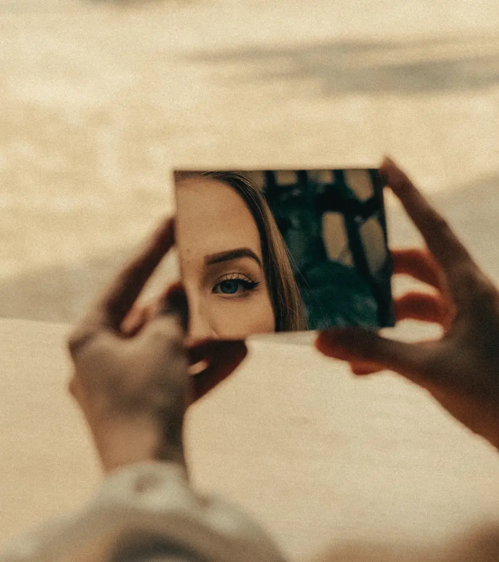 Vrouw die in een spiegel kijkt, symbool voor zelfreflectie bij het stoppen met alcohol of drugs.