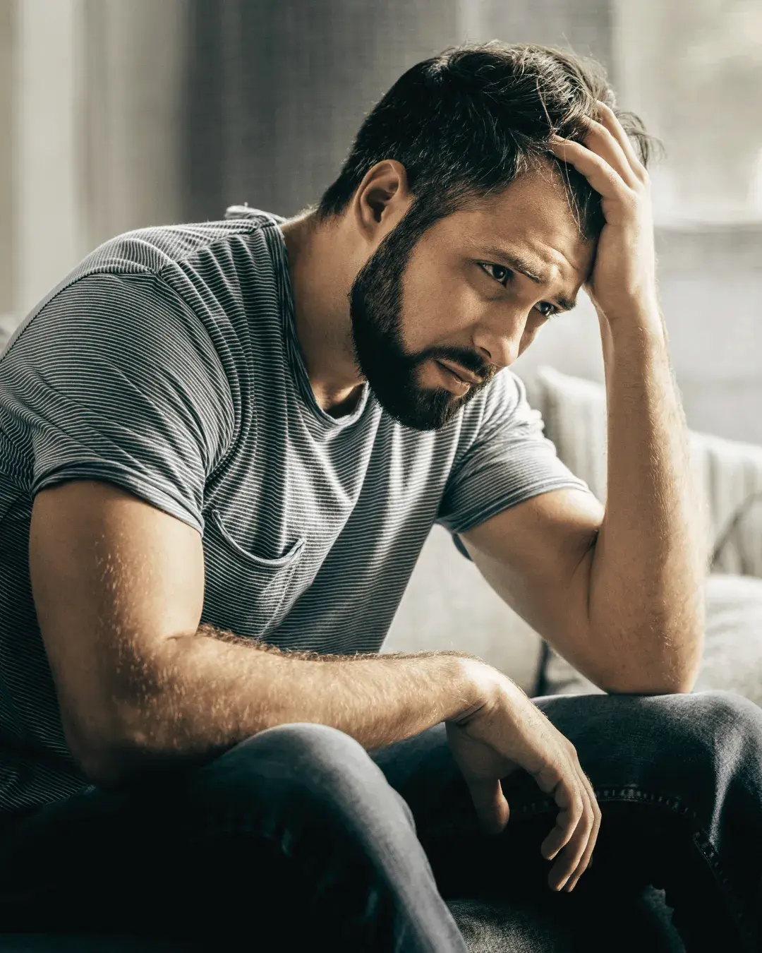 Man die vermoeid en bezorgd op de bank zit, als illustratie van innerlijke onrust door middelengebruik.