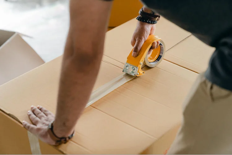 A man is packing a carton box with yellow tape