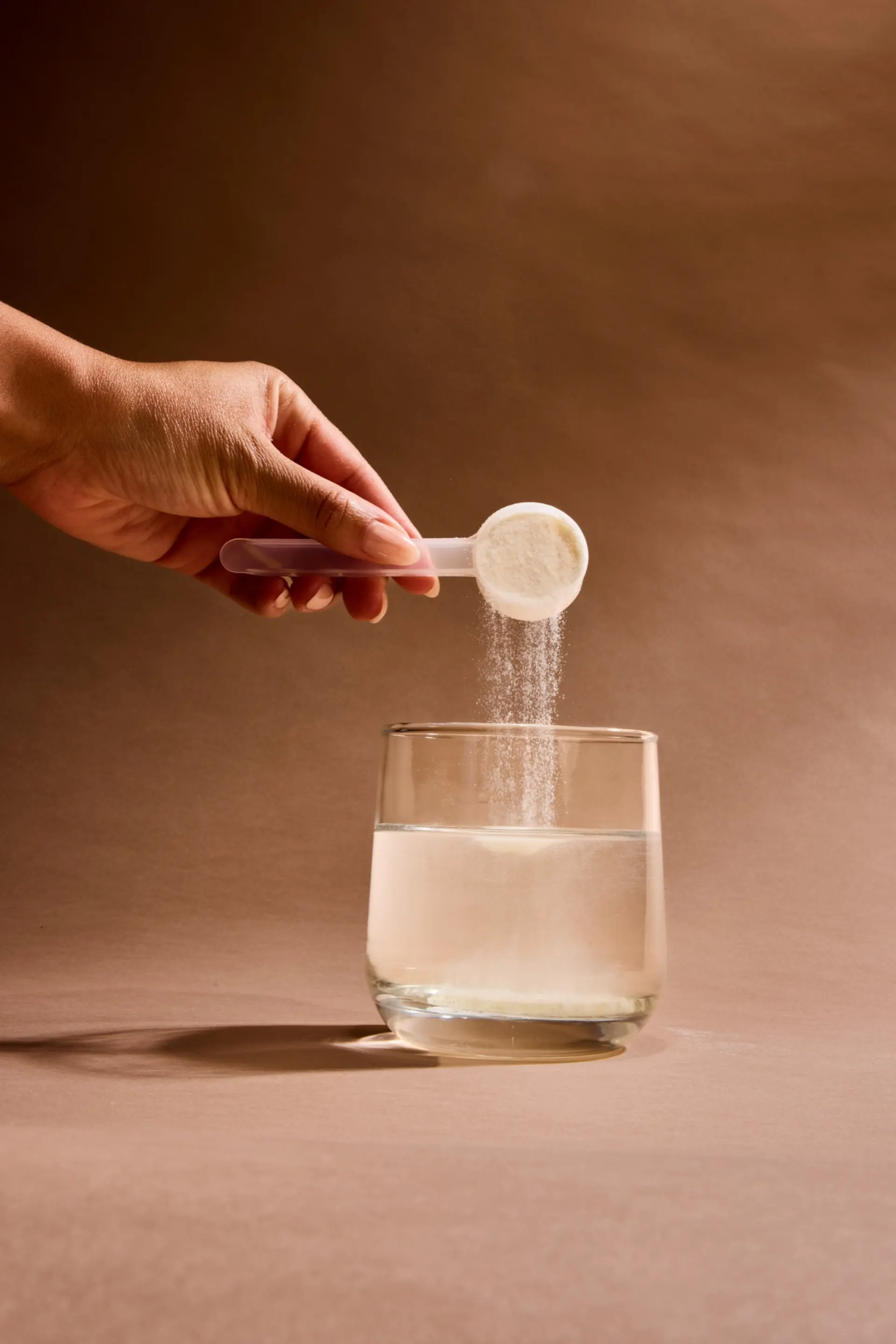 Hand pouring a scoop of protein powder into a glass of water