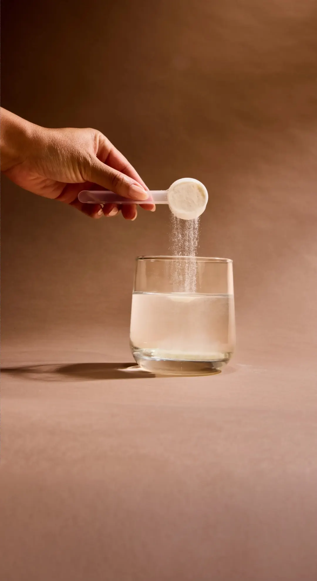 Hand pouring a scoop of protein powder into a glass of water