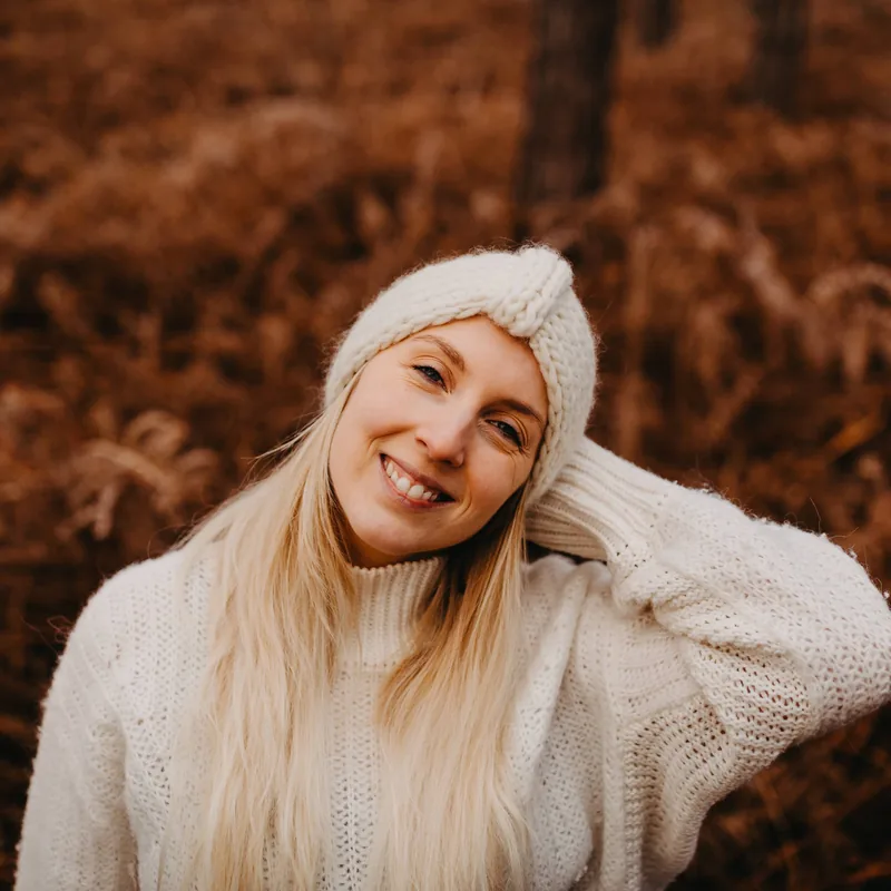 Shannen Rasking in een witte trui en muts, lachend in een herfstbos