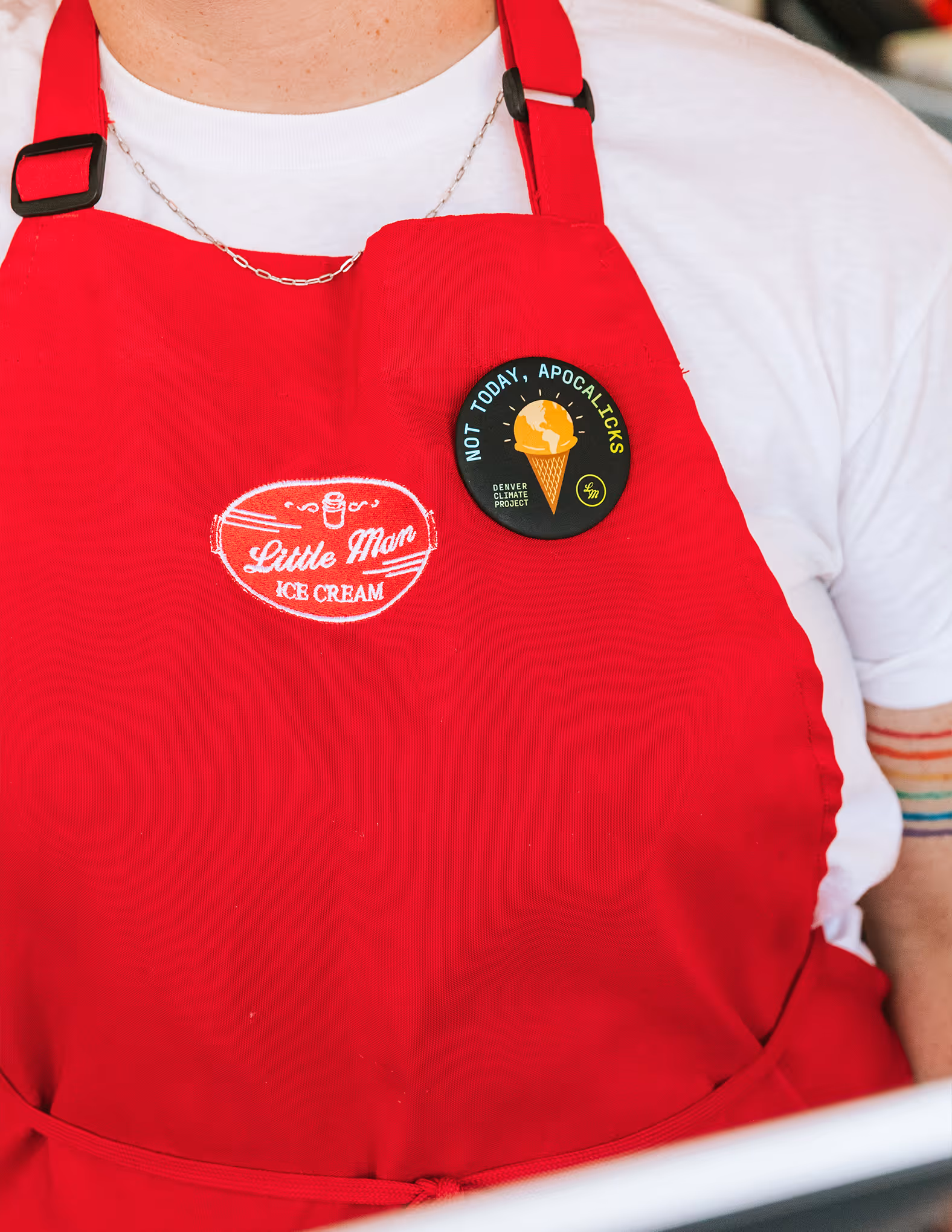 close up of a employee wearing a little man ice cream apron with a Denver Climate Project button highlighting the Not today, apocalicks flavor.